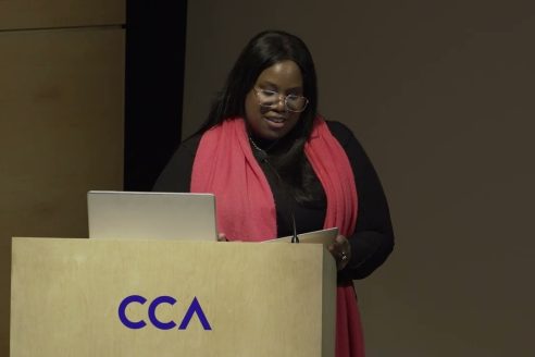 Mary Louise Richards stands on stage at a podium, giving a lecture
